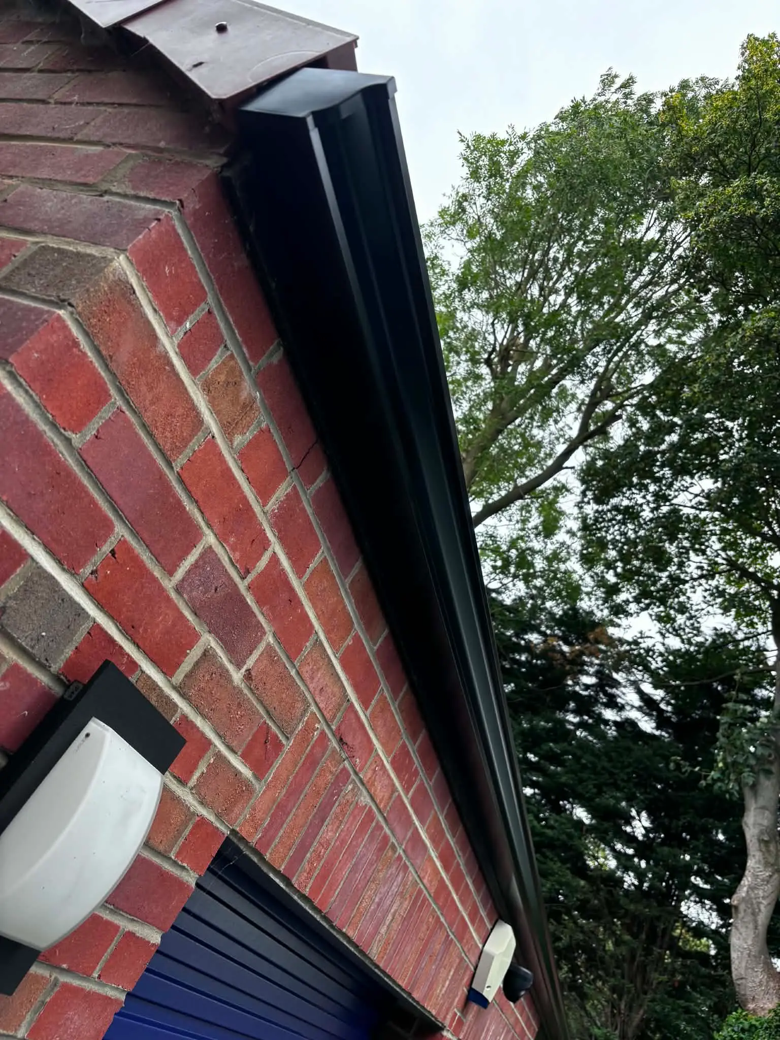 New black guttering with a clean finished end detail on a brick commercial building after installation