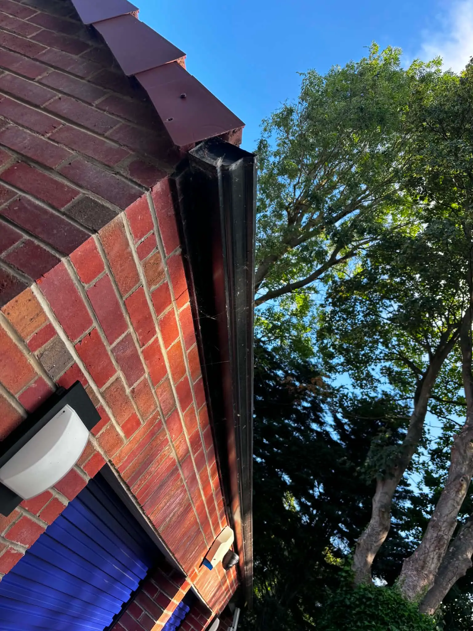 Older black guttering with a worn and untidy end detail on a brick commercial building before replacement