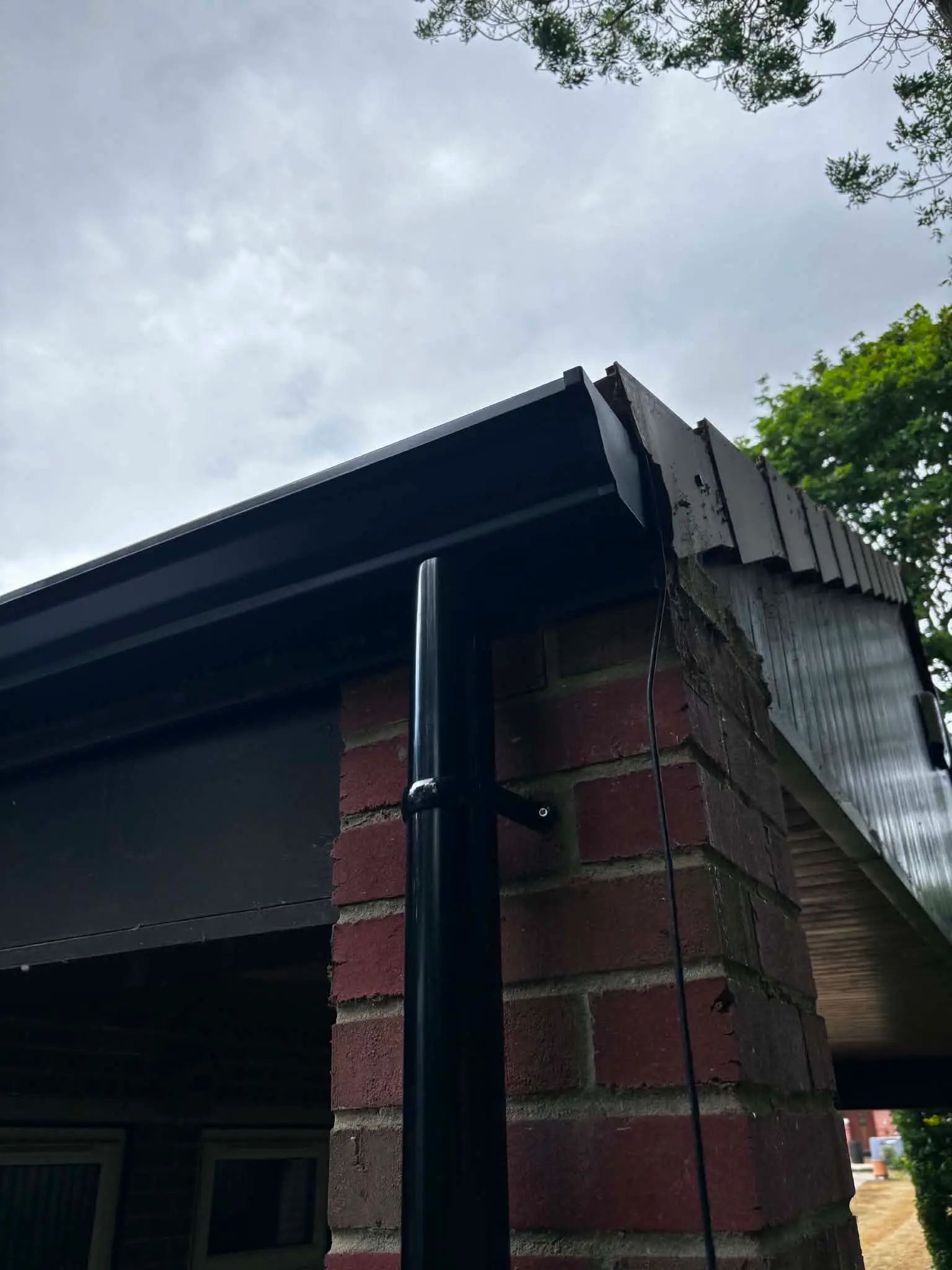 Completed black guttering and securely fitted downpipe on a brick outbuilding