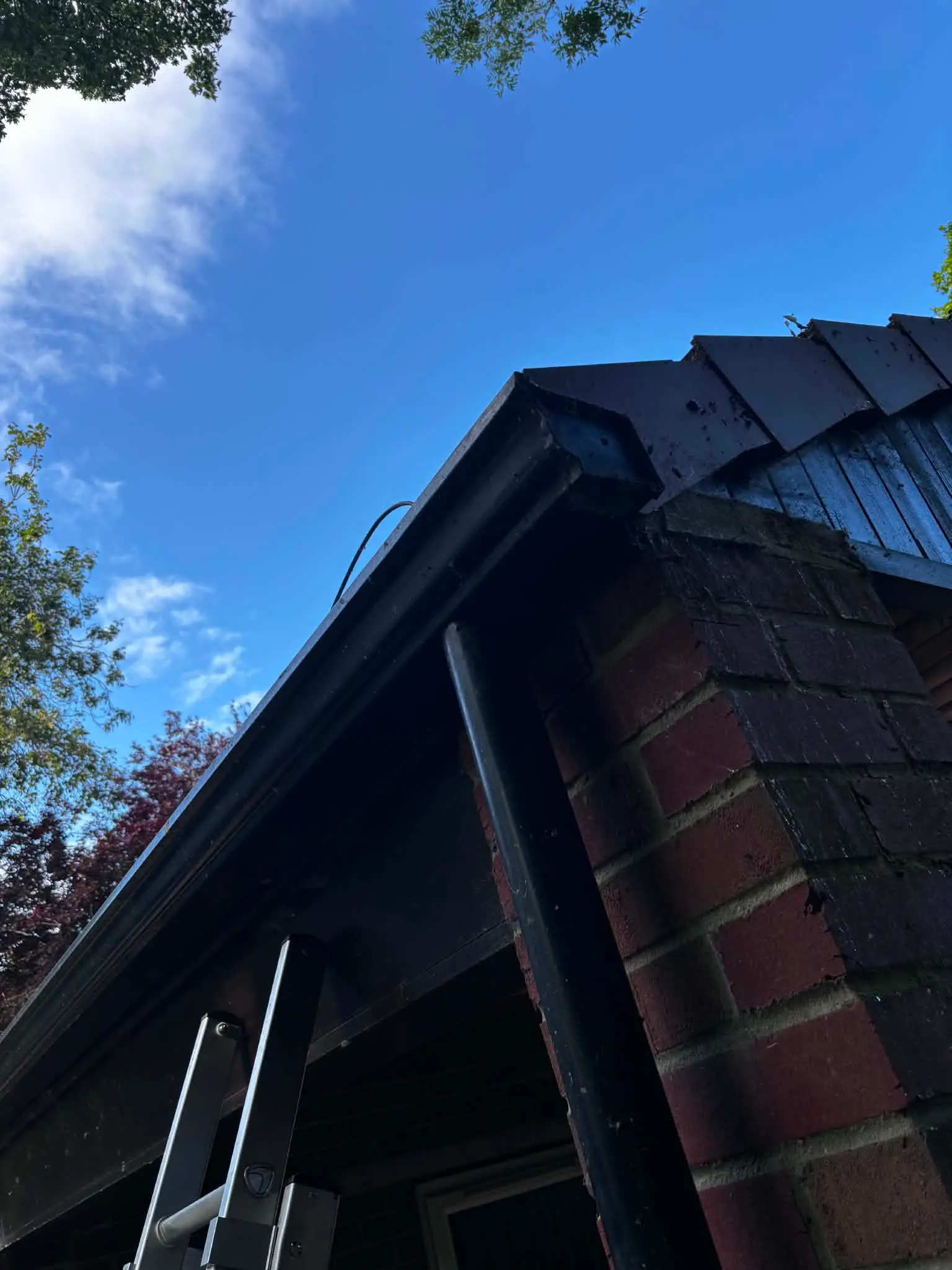 Older black guttering and roof edge on a brick outbuilding before improvement work