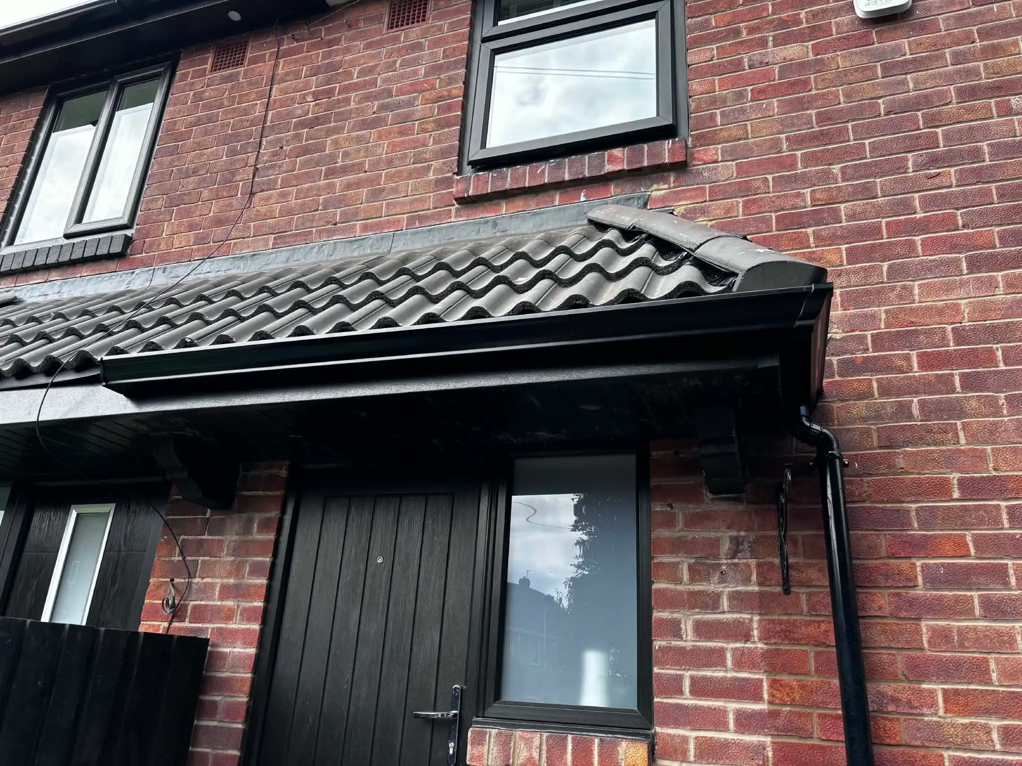 Completed black guttering and downpipe installation on a brick house entrance porch